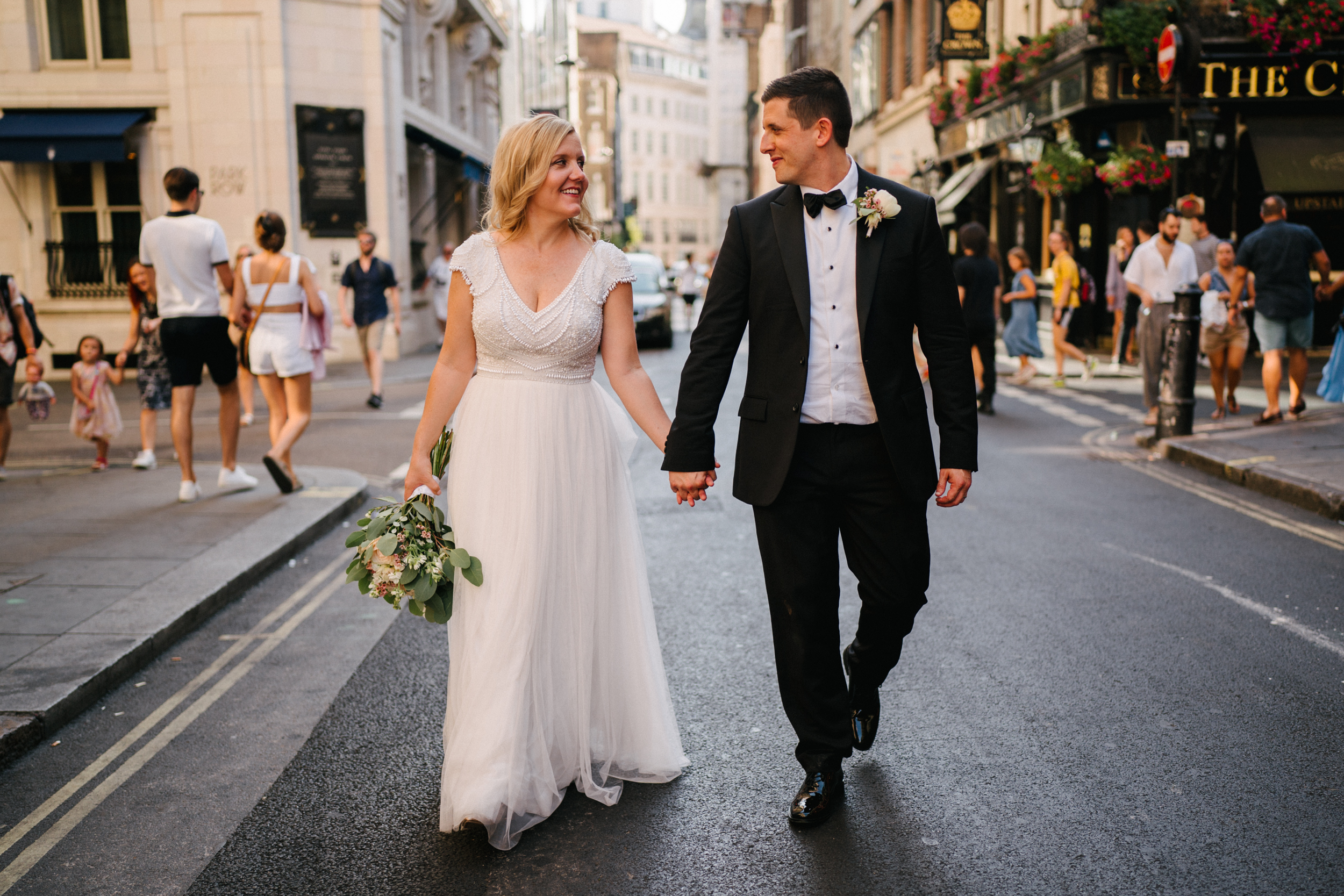 A bride and groom walking through Soho in London during their wedding at Hotel Cafe Royal. 