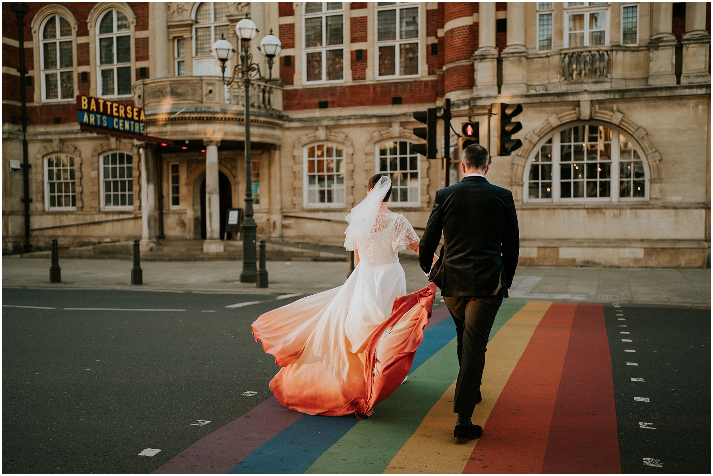 A couple walks across a rainbow road towards the Battersea Arts Centre.